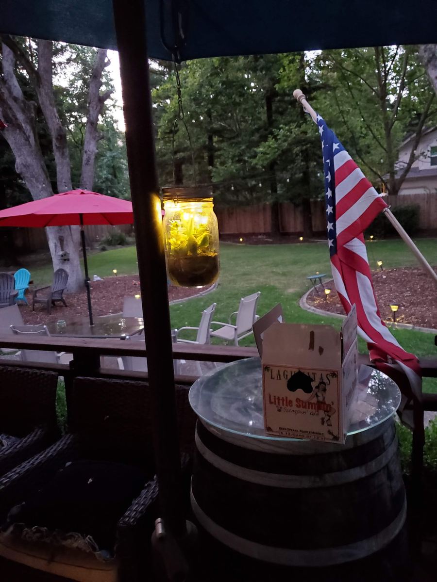 Glowing lantern jar hanging from a patio umbrella in a backyard at dusk